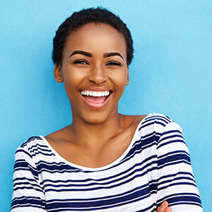 young woman in striped shirt smiling with her new porcelain veneers in front of a blue background
