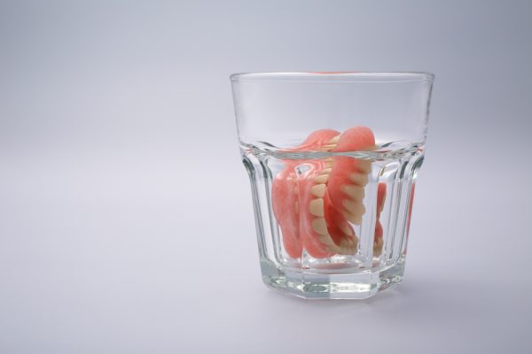 dentures soaking in cleaner in a glass